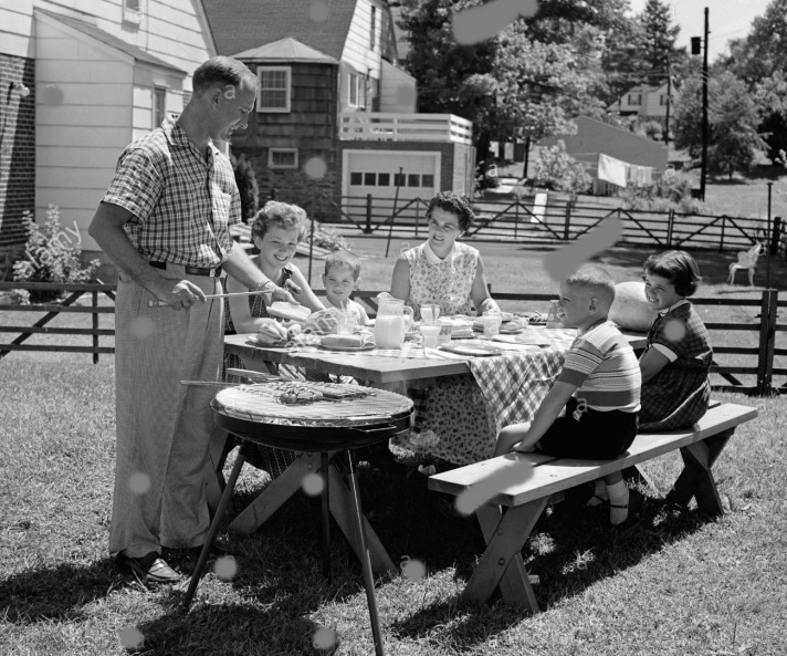 1950s-family-in-backyard-cooking-hot-dogs-sitting-at-picnic-table-AAKTPY